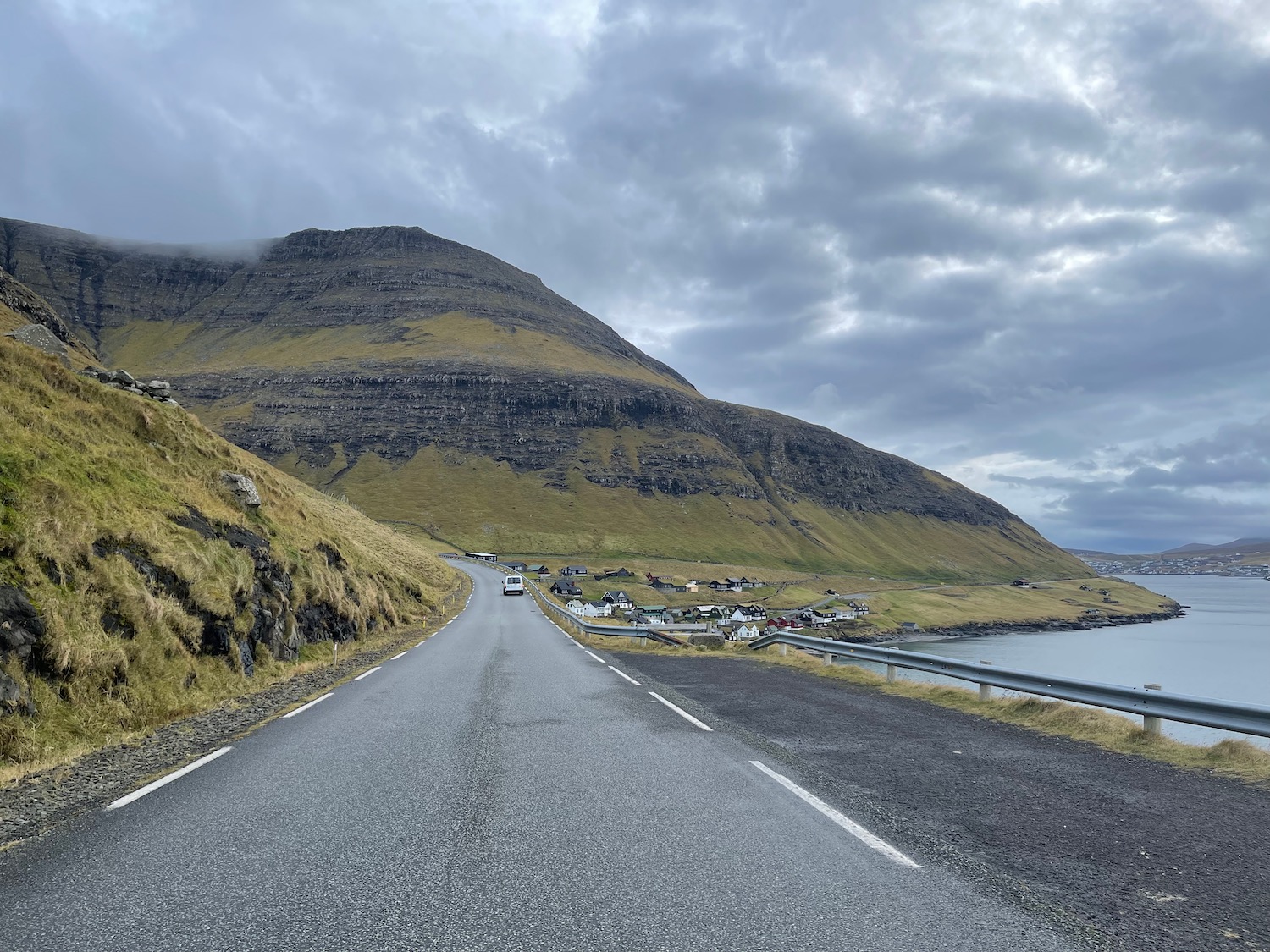 a road with a body of water and a hill with houses on it