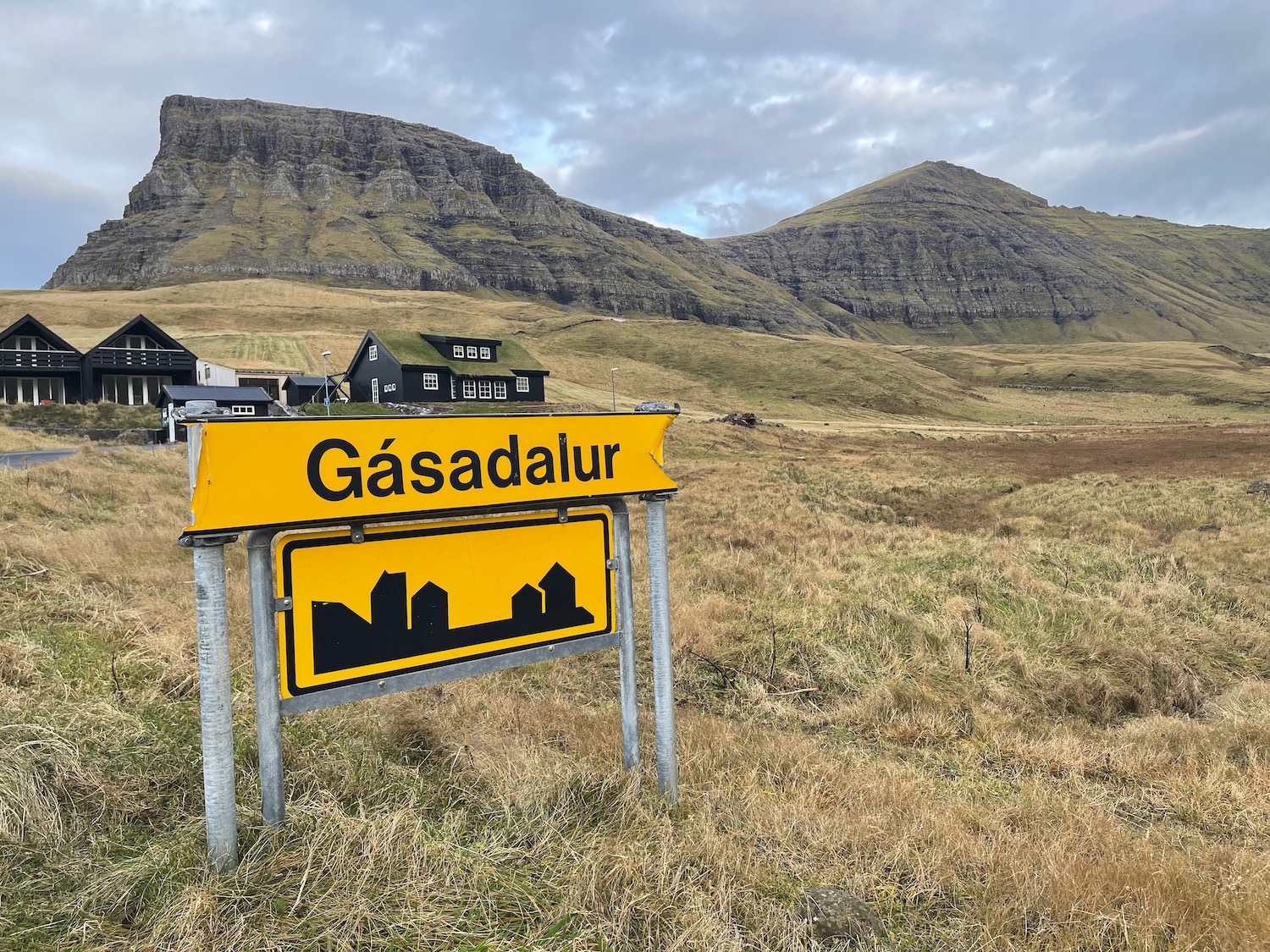 a yellow sign in a field with mountains in the background