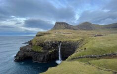 a waterfall on a cliff above water