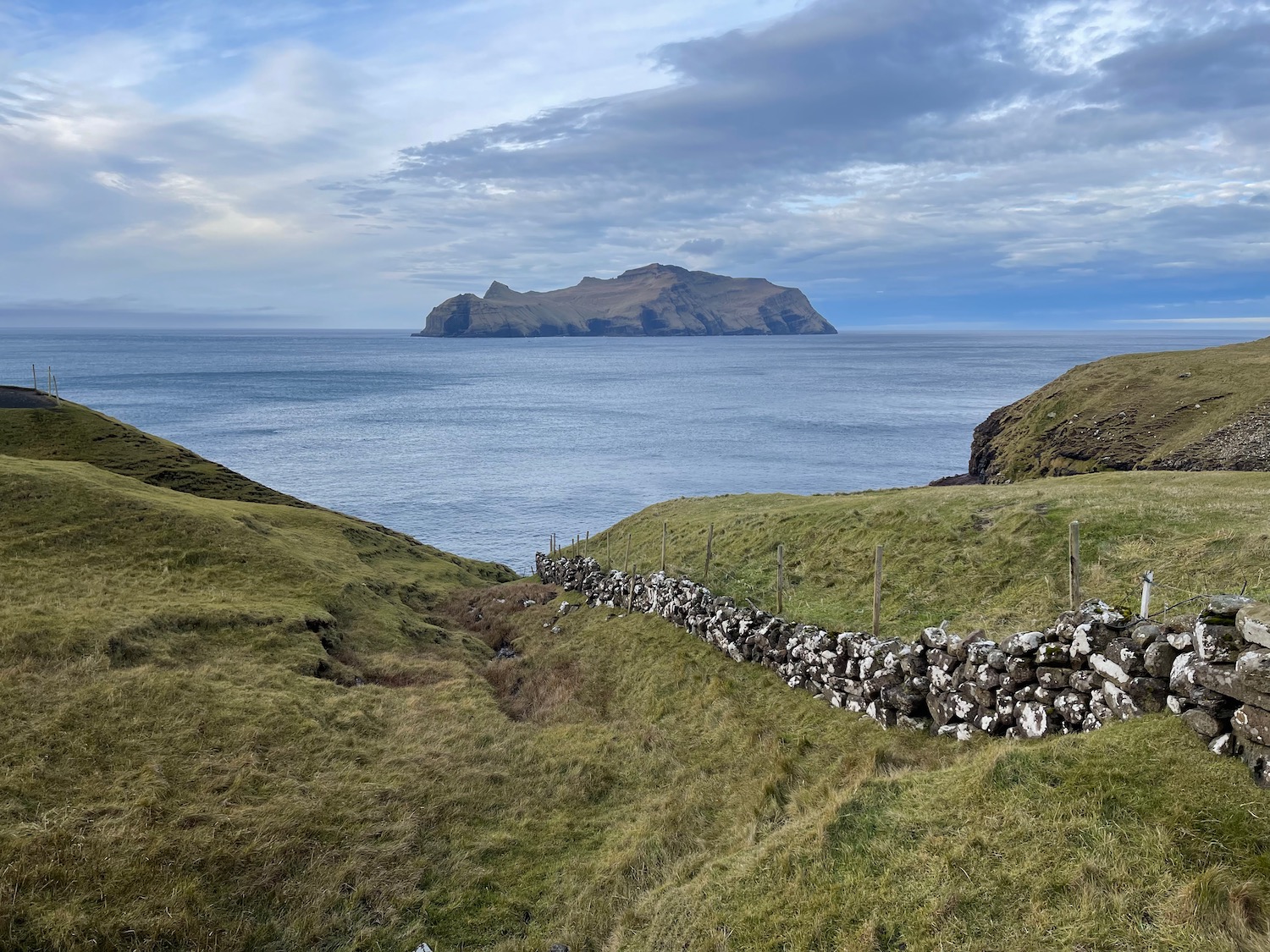 a grassy hill with a fence and a rock wall by the water