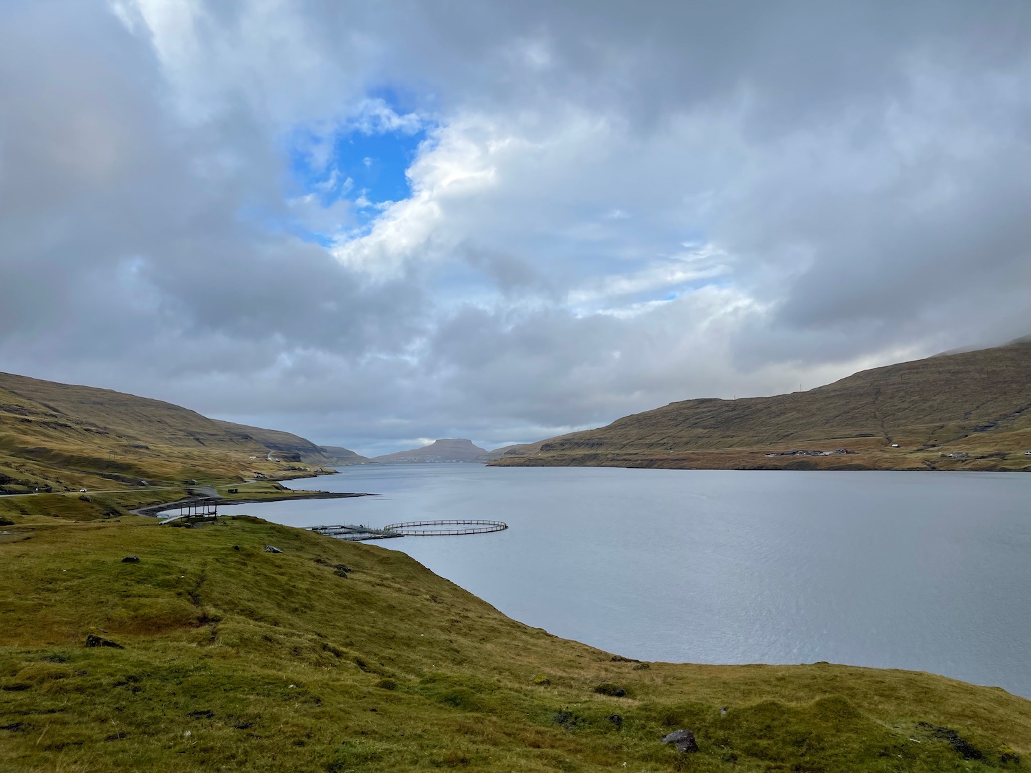 a body of water with hills and a cloudy sky