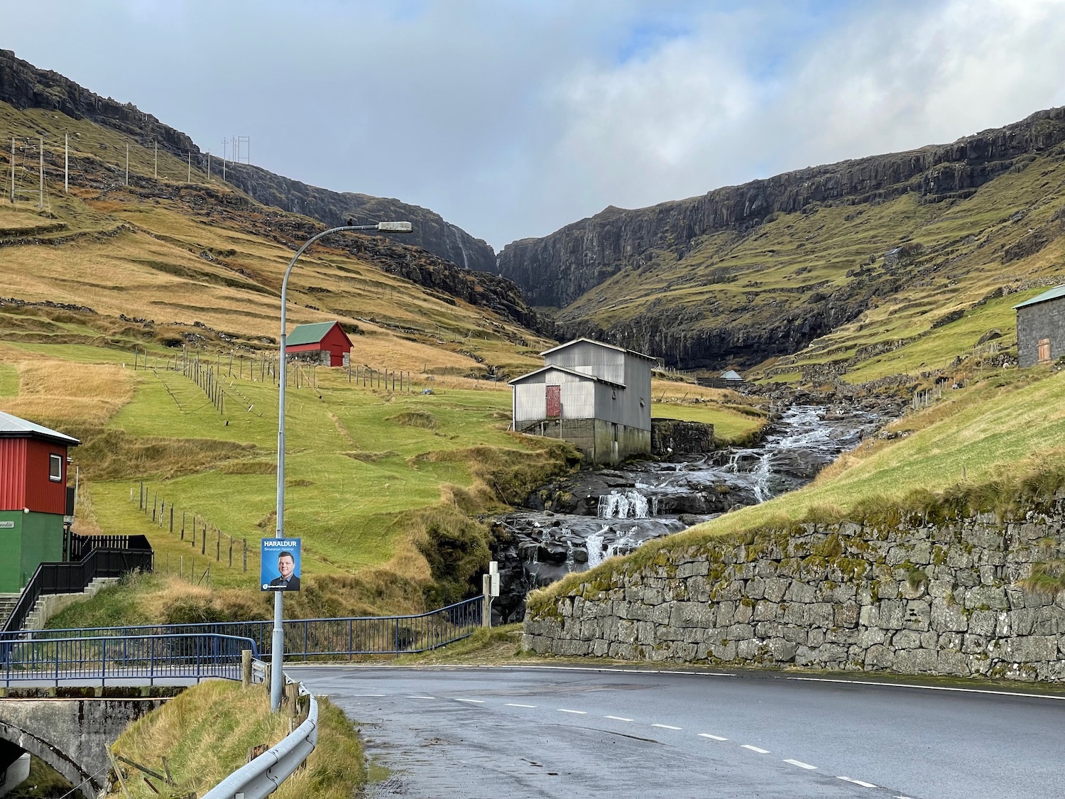 a road with a small building and a stream in the middle of a valley