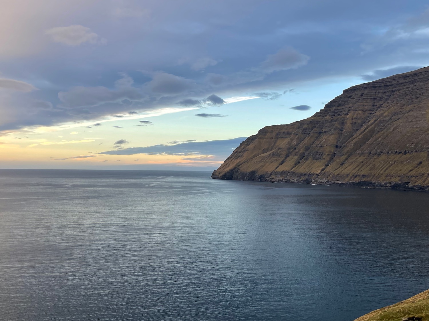 a body of water with a hill and a cloudy sky