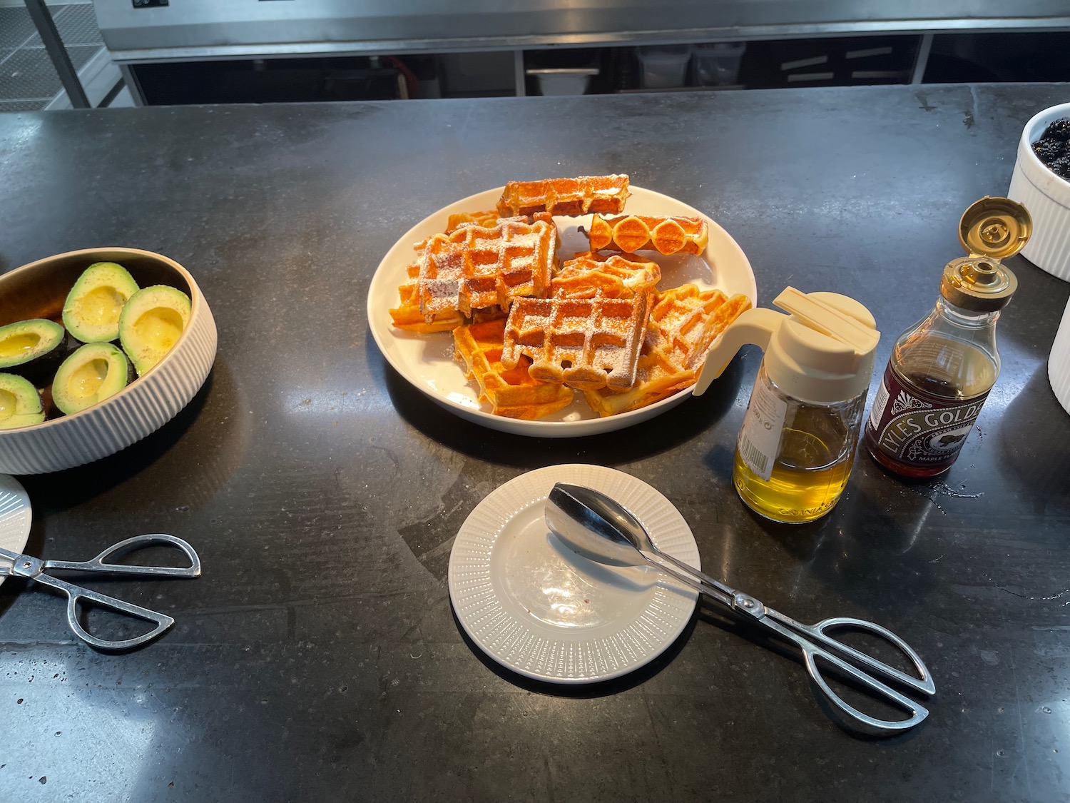 a plate of waffles and a bowl of avocado on a black counter