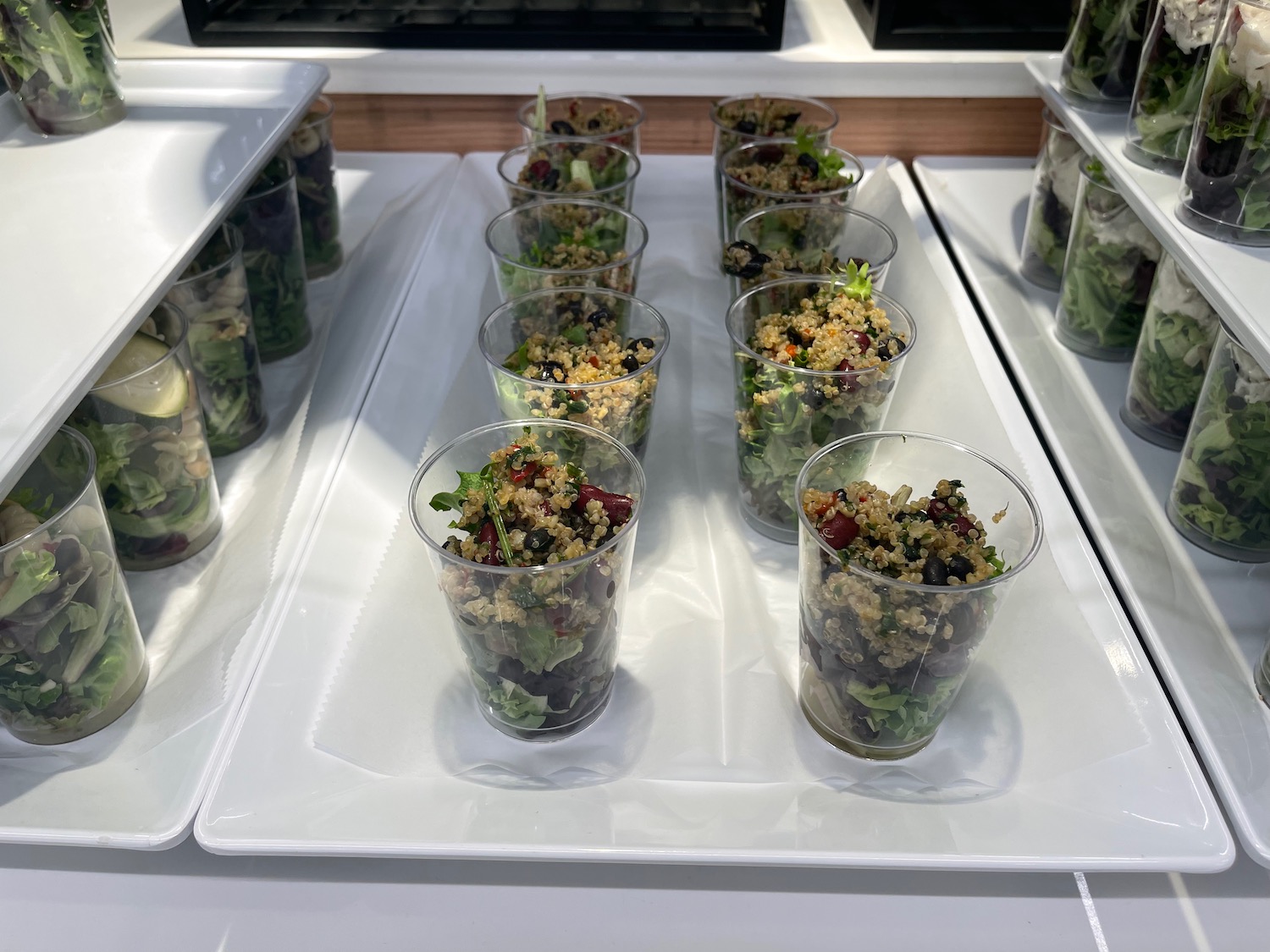 a row of plastic cups with salad on a white tray