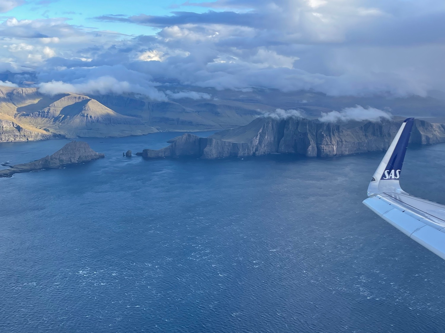 an airplane wing over water with mountains in the background