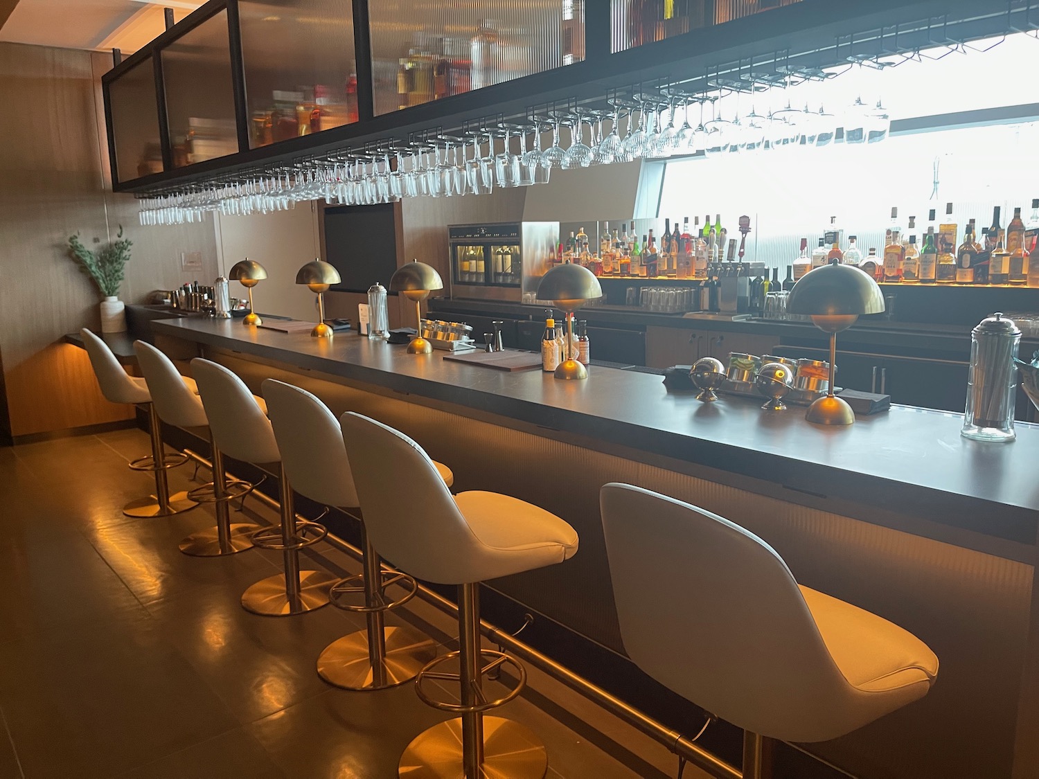 a bar with white chairs and a bar with a row of glasses