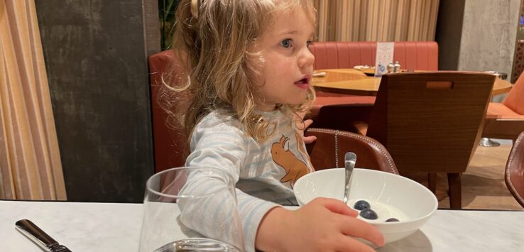 a girl sitting at a table with a bowl of food