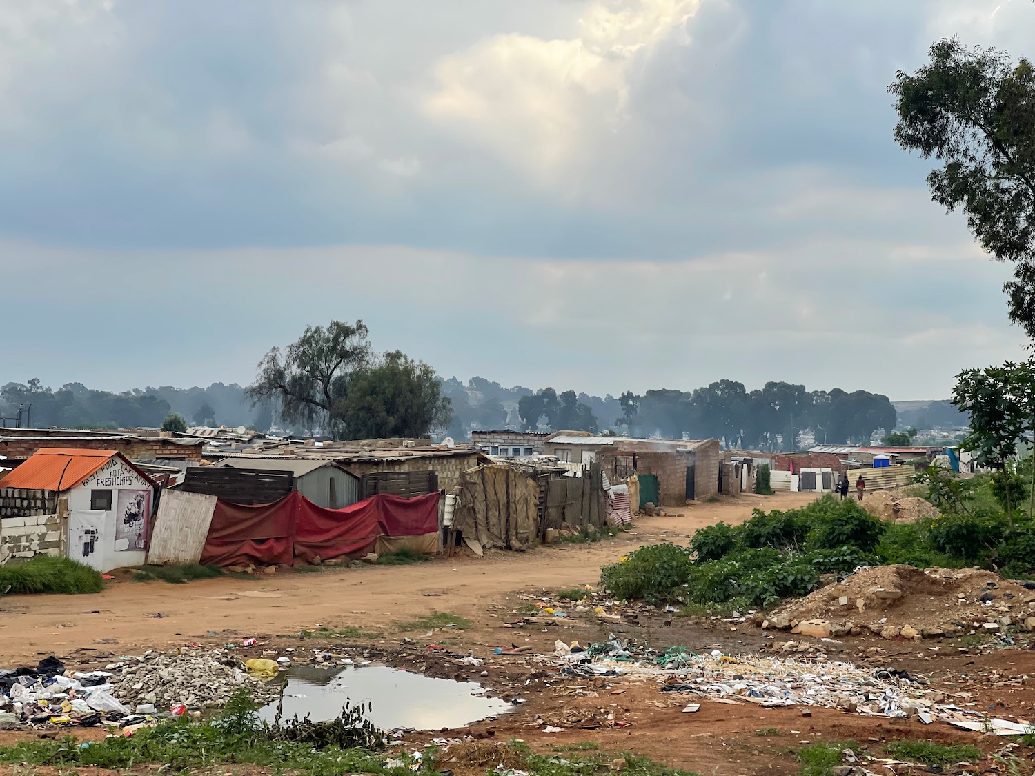 a dirt road with a group of houses and a puddle of water