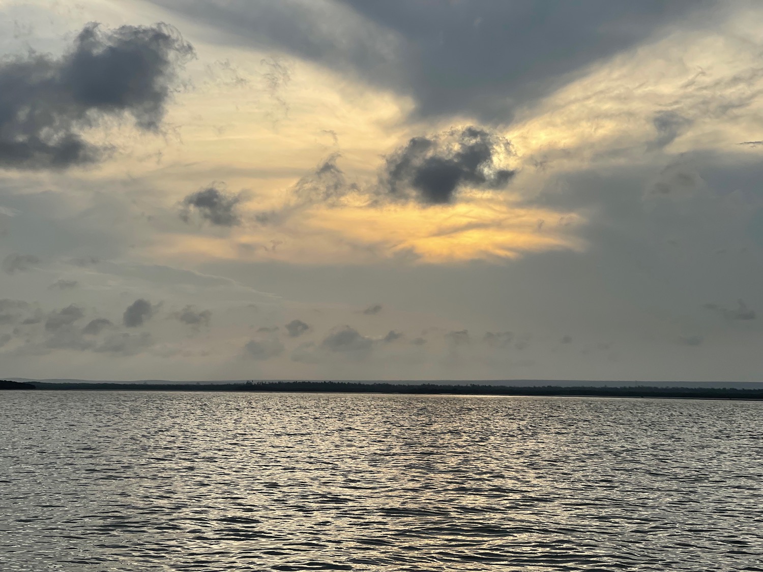 a body of water with clouds and a sun shining through the clouds