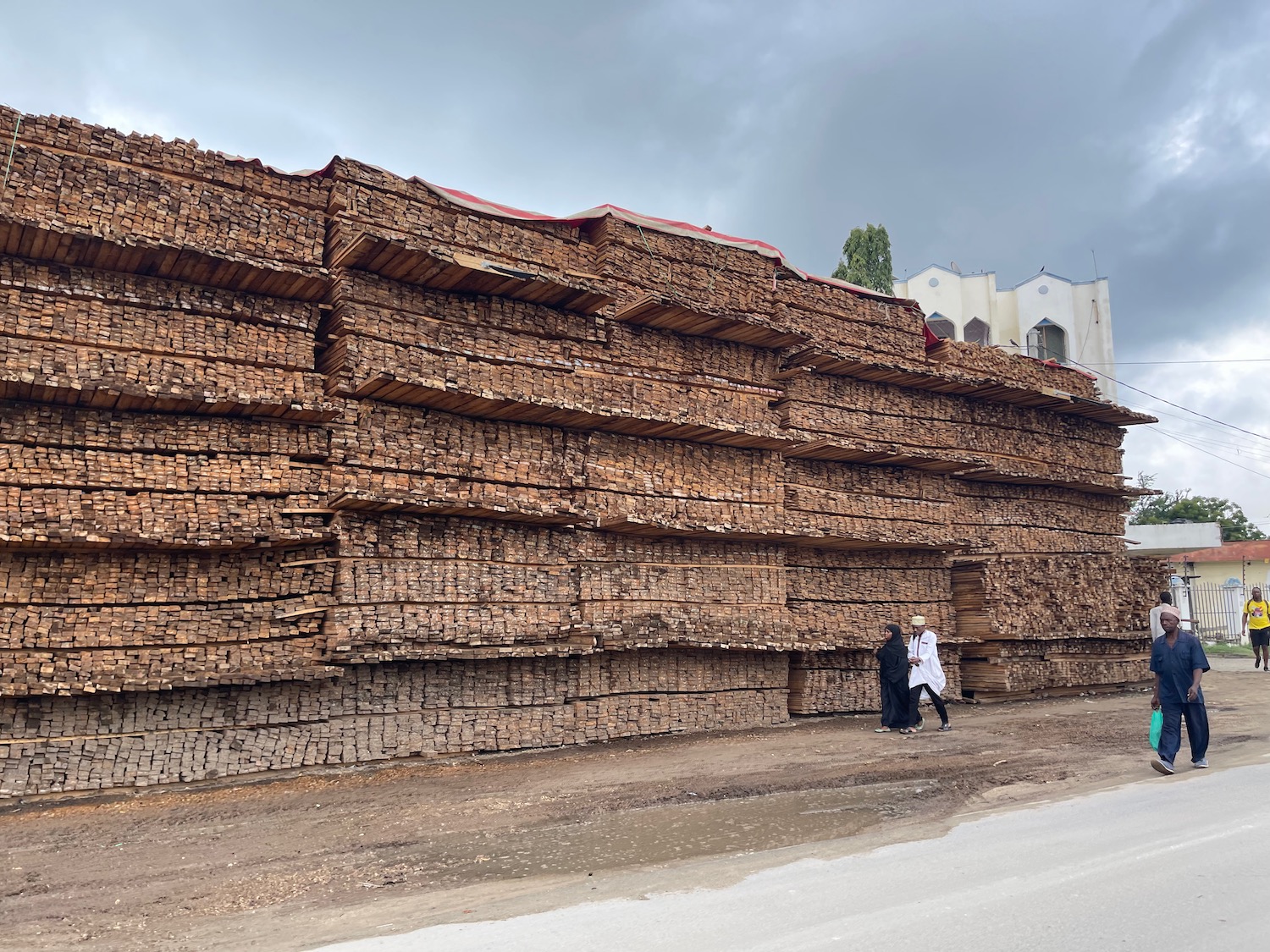 a couple of people walking next to a large stack of wood