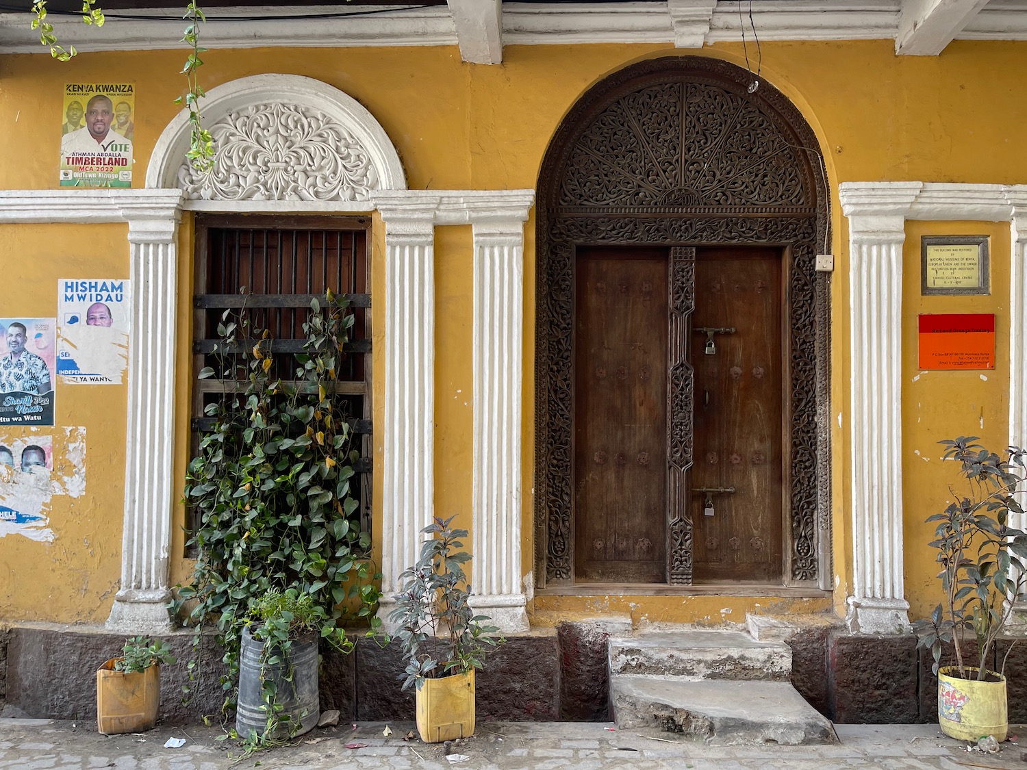 a yellow building with a door and a plant