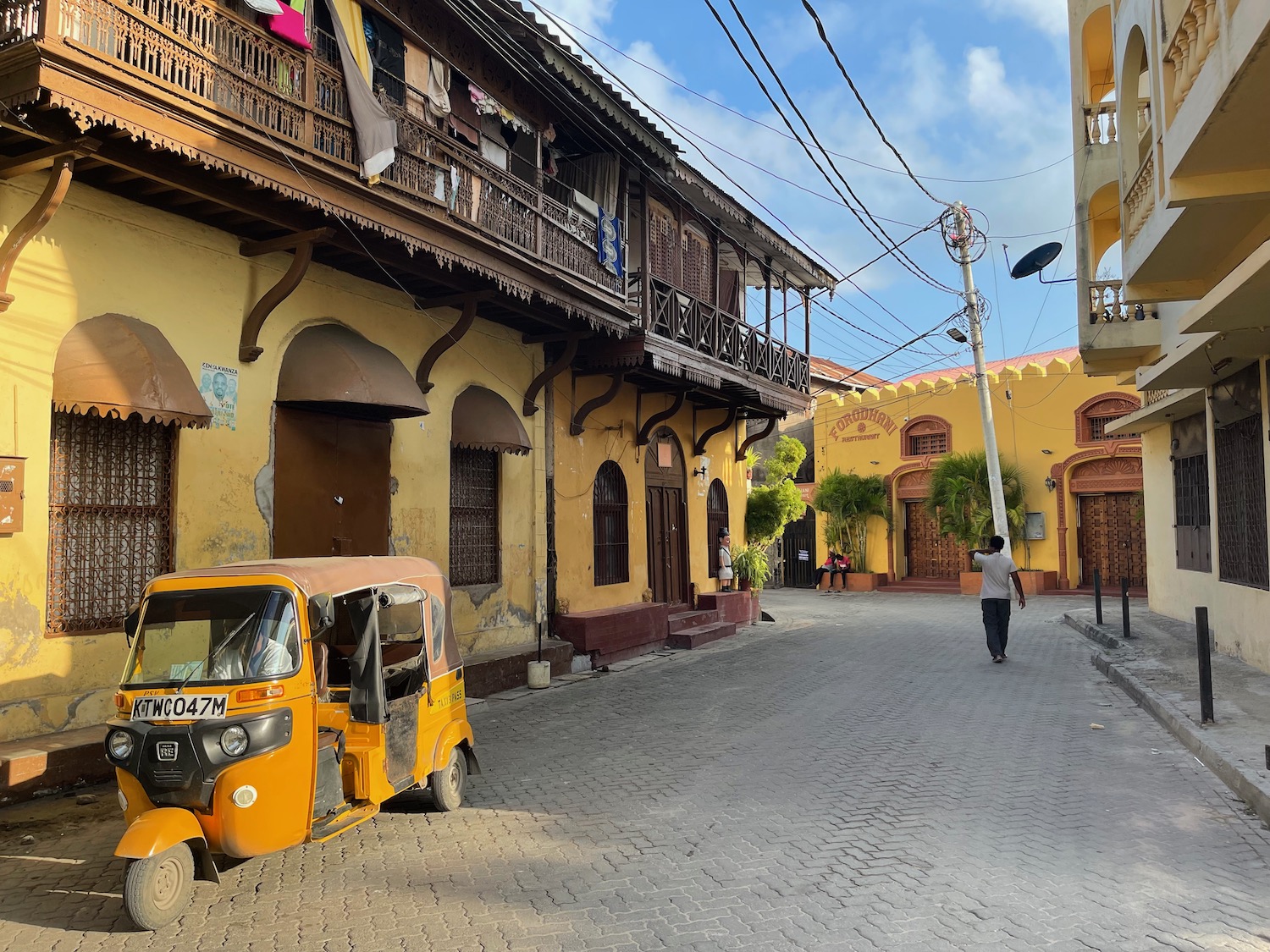 a yellow vehicle parked on a street with buildings and a person walking