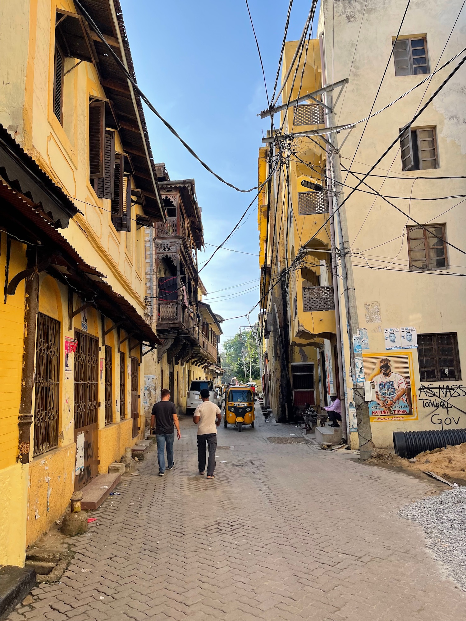 a group of people walking down a narrow street with buildings and power lines