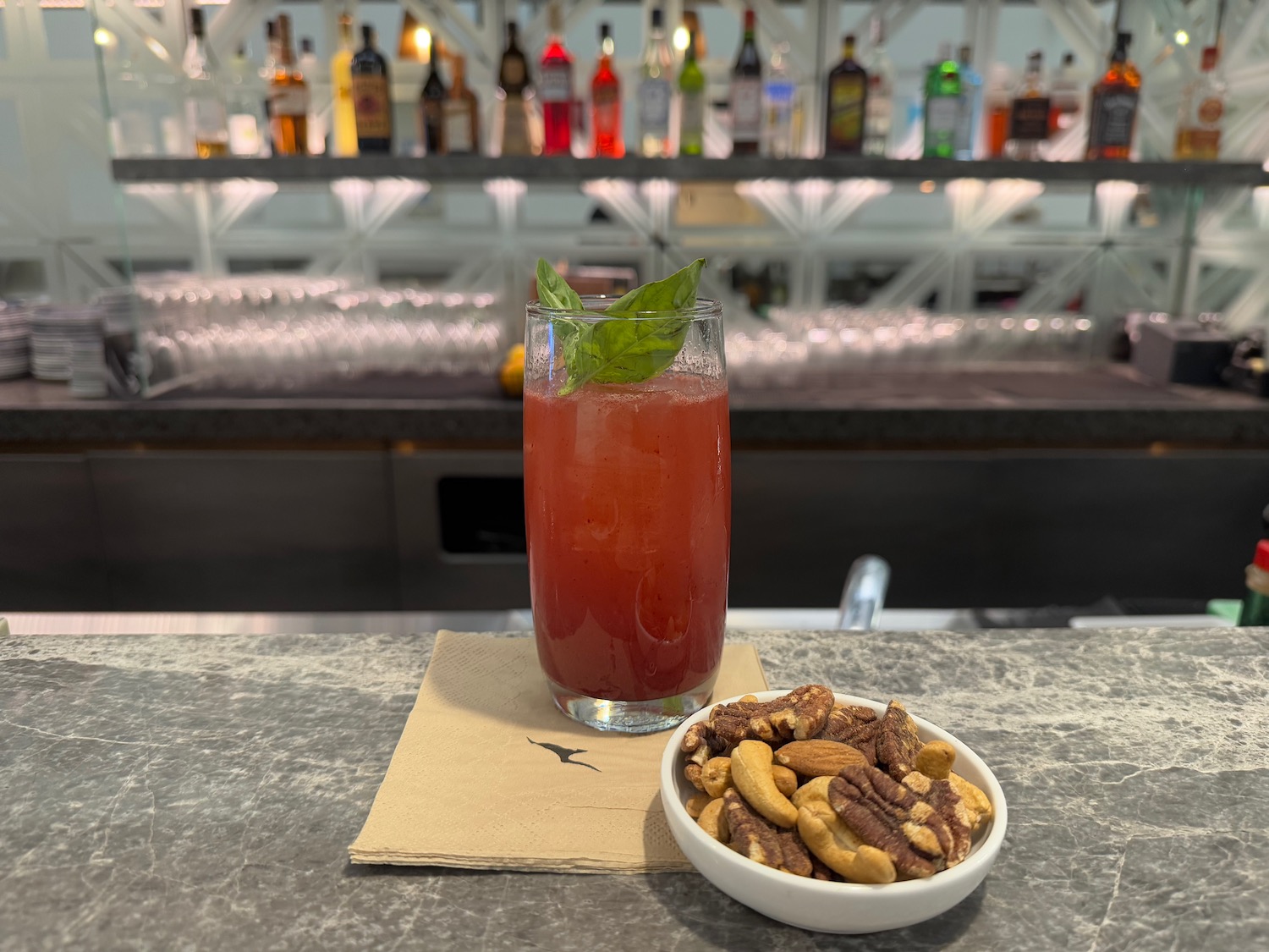 a glass of red liquid next to a bowl of nuts
