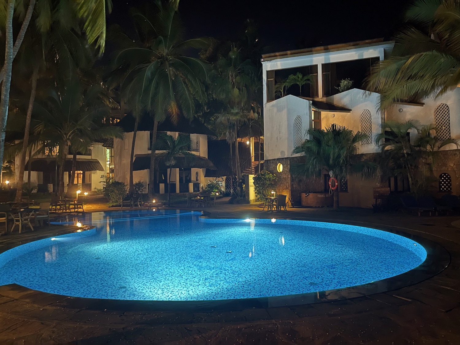 a pool with palm trees and buildings at night