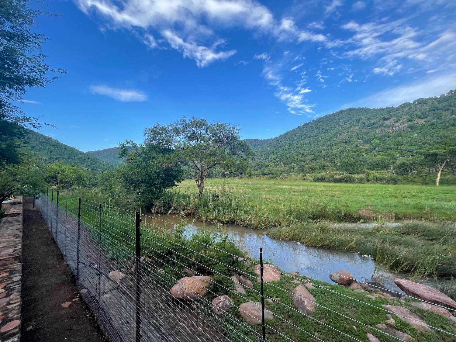 a fence and a river with trees and mountains in the background