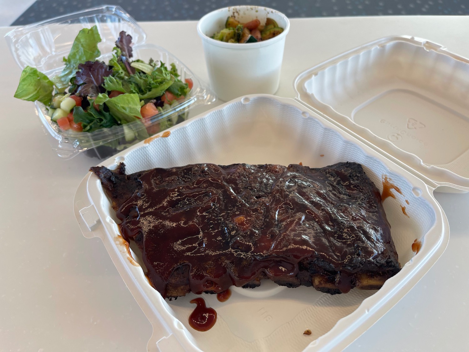 a styrofoam container with ribs and salad