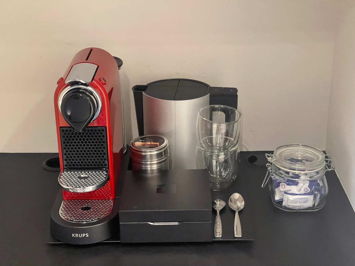 a red coffee machine and silverware on a black surface