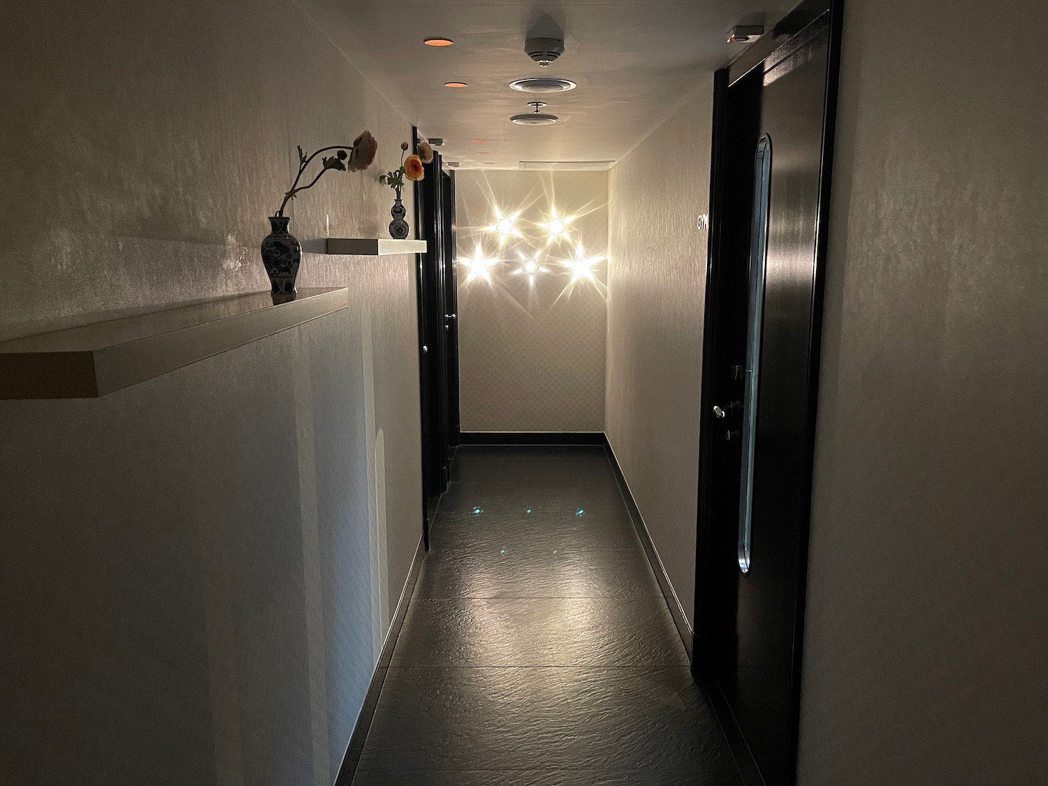 a hallway with a black door and a vase of flowers