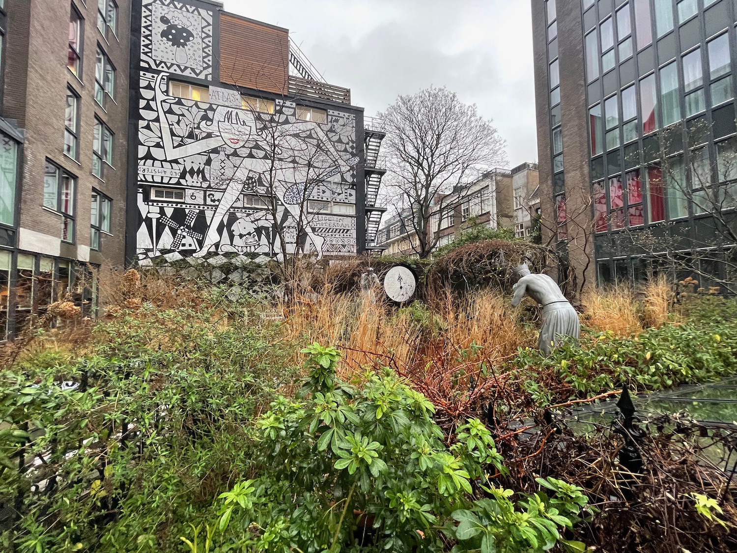 a garden with a statue and a clock on the side of a building