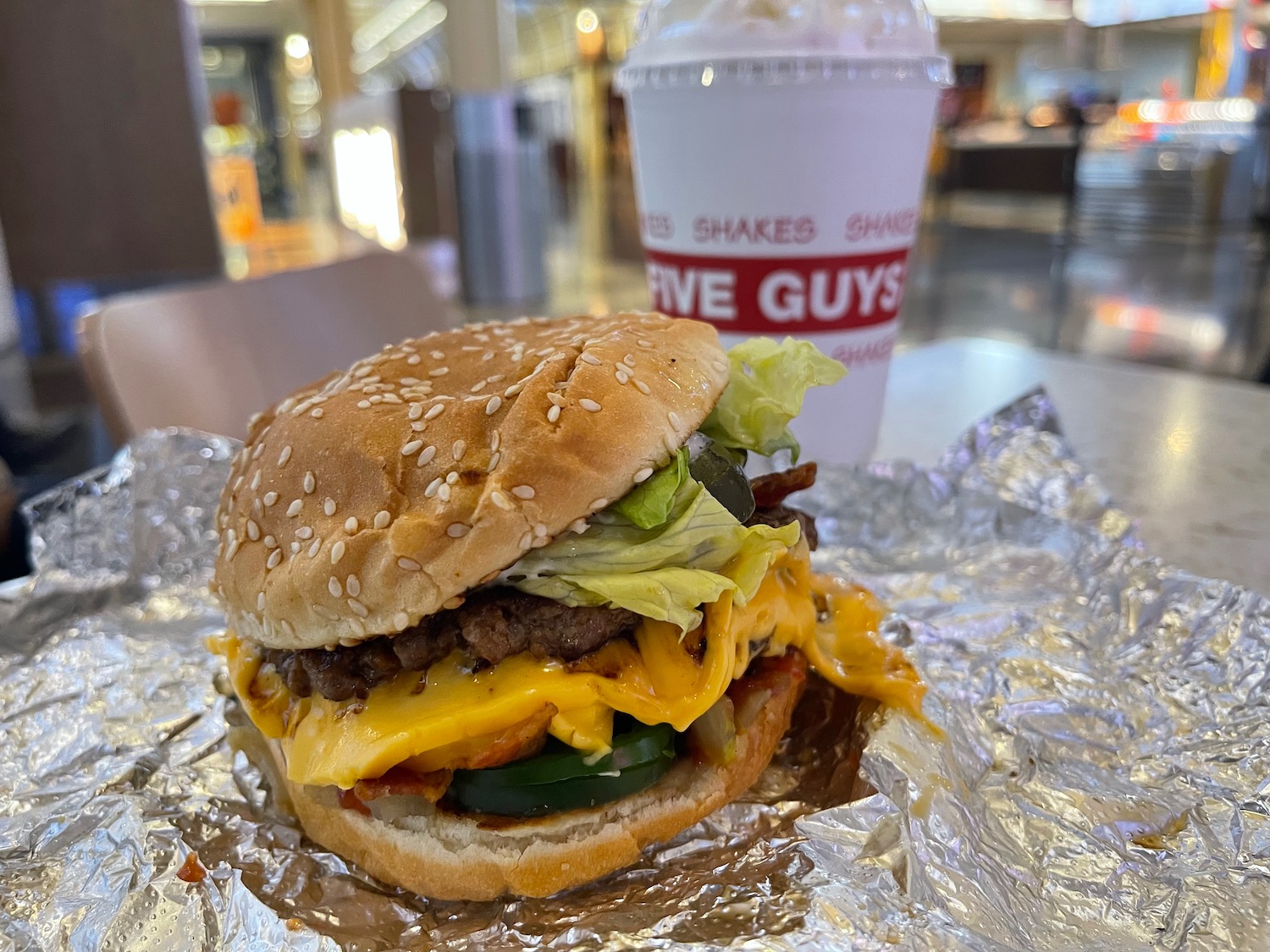 a cheeseburger on foil with a drink in the background