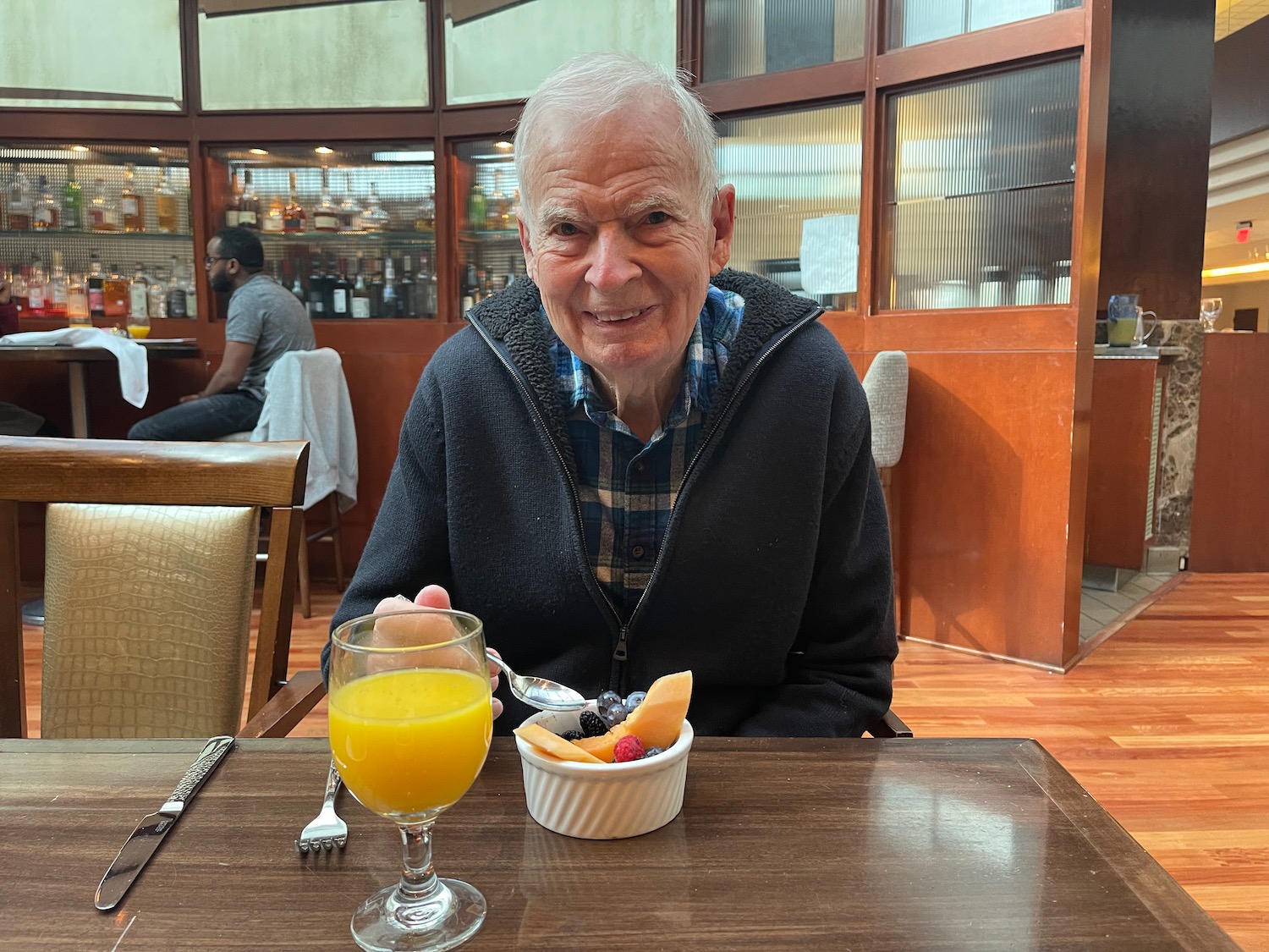 an old man sitting at a table with a bowl of fruit and a glass of orange juice