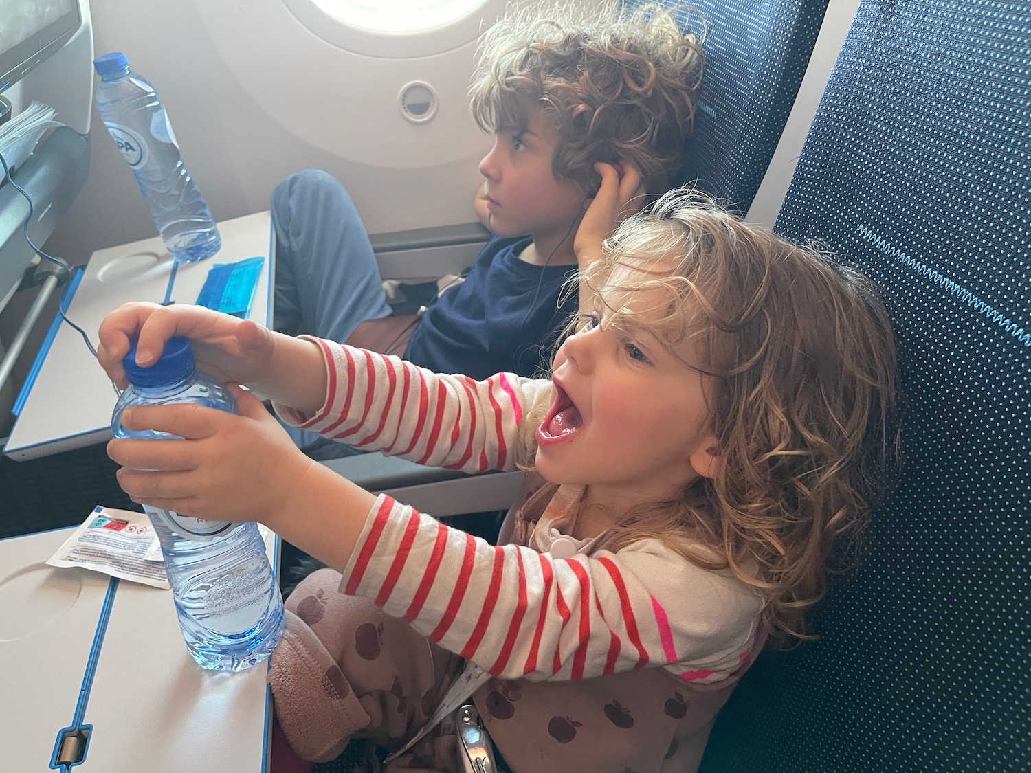 a boy and girl sitting on an airplane with a bottle of water