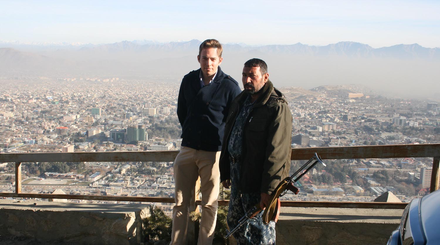 two men standing on a ledge with a city in the background