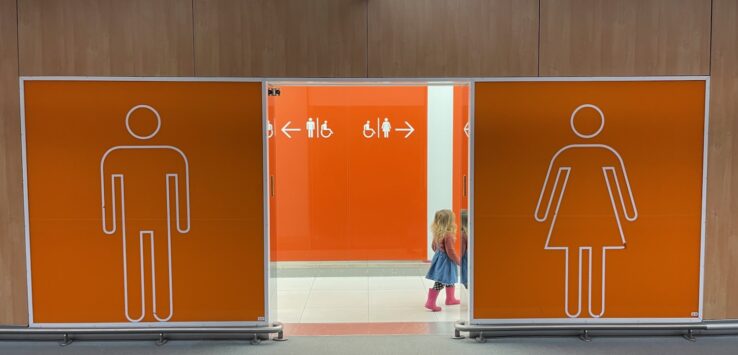 a girl standing in front of a man and woman toilet