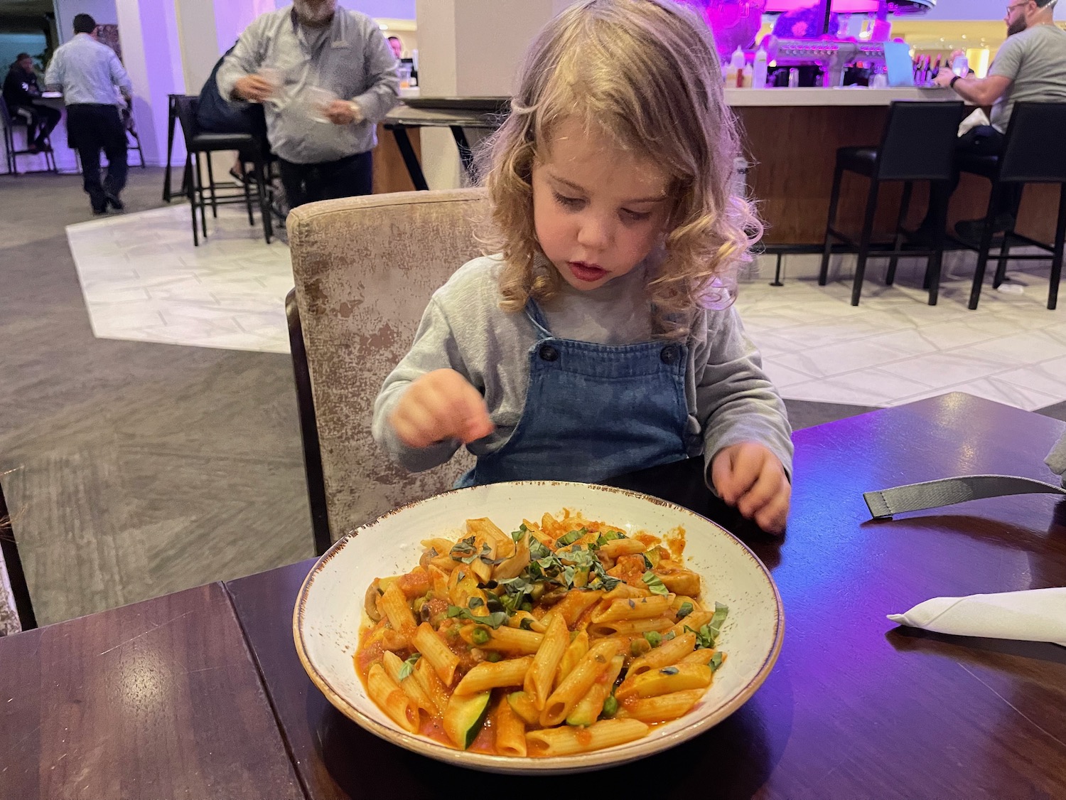 a girl sitting at a table with a plate of pasta