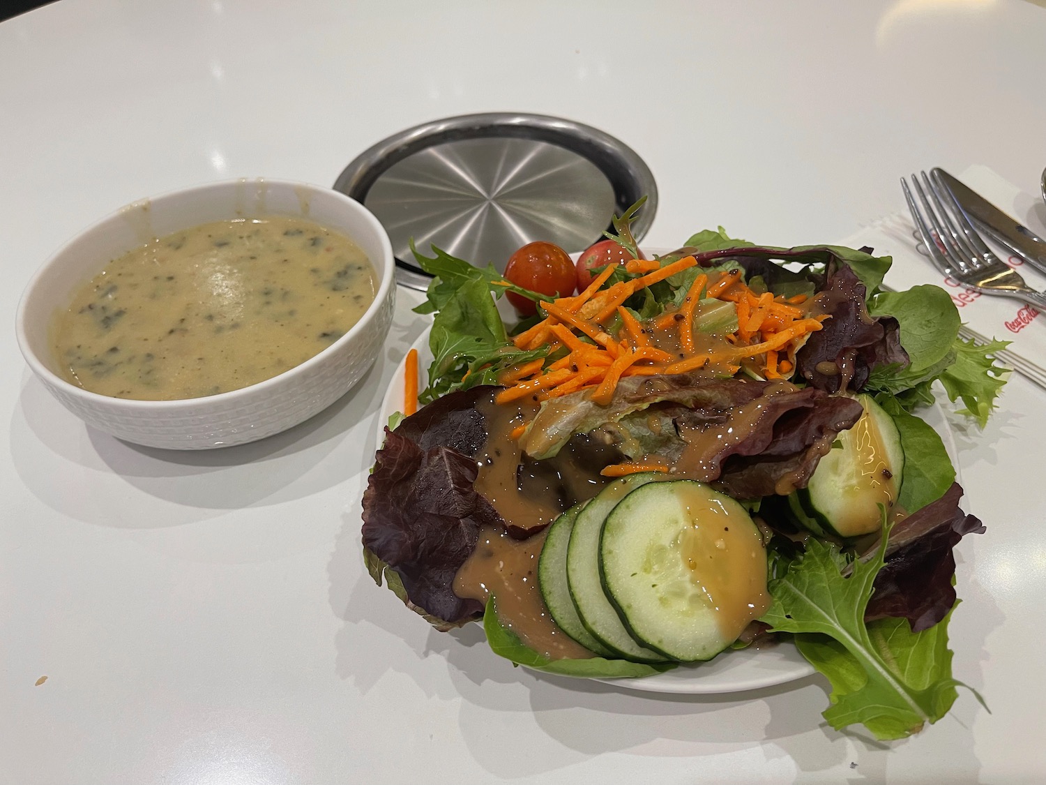 a plate of salad with a bowl of soup and fork