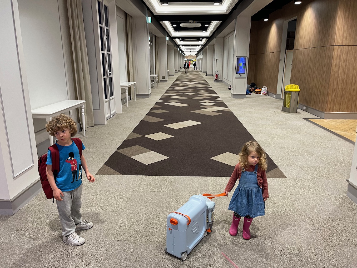 a boy and girl standing in a hallway with luggage
