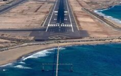 an airport runway with a body of water and mountains in the background