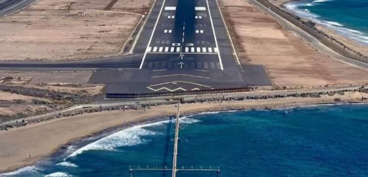 an airport runway with a body of water and mountains in the background