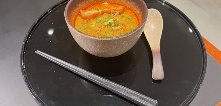 a bowl of soup and chopsticks on a black tray