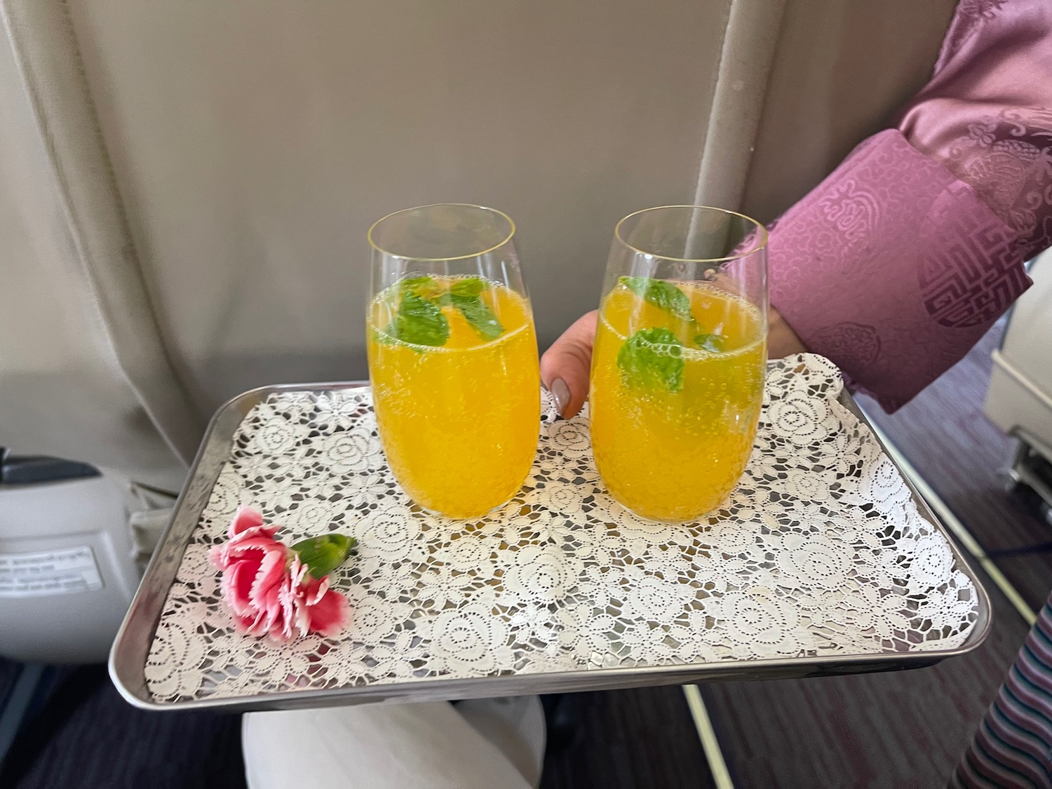 a tray with two glasses of yellow liquid and mint leaves on it