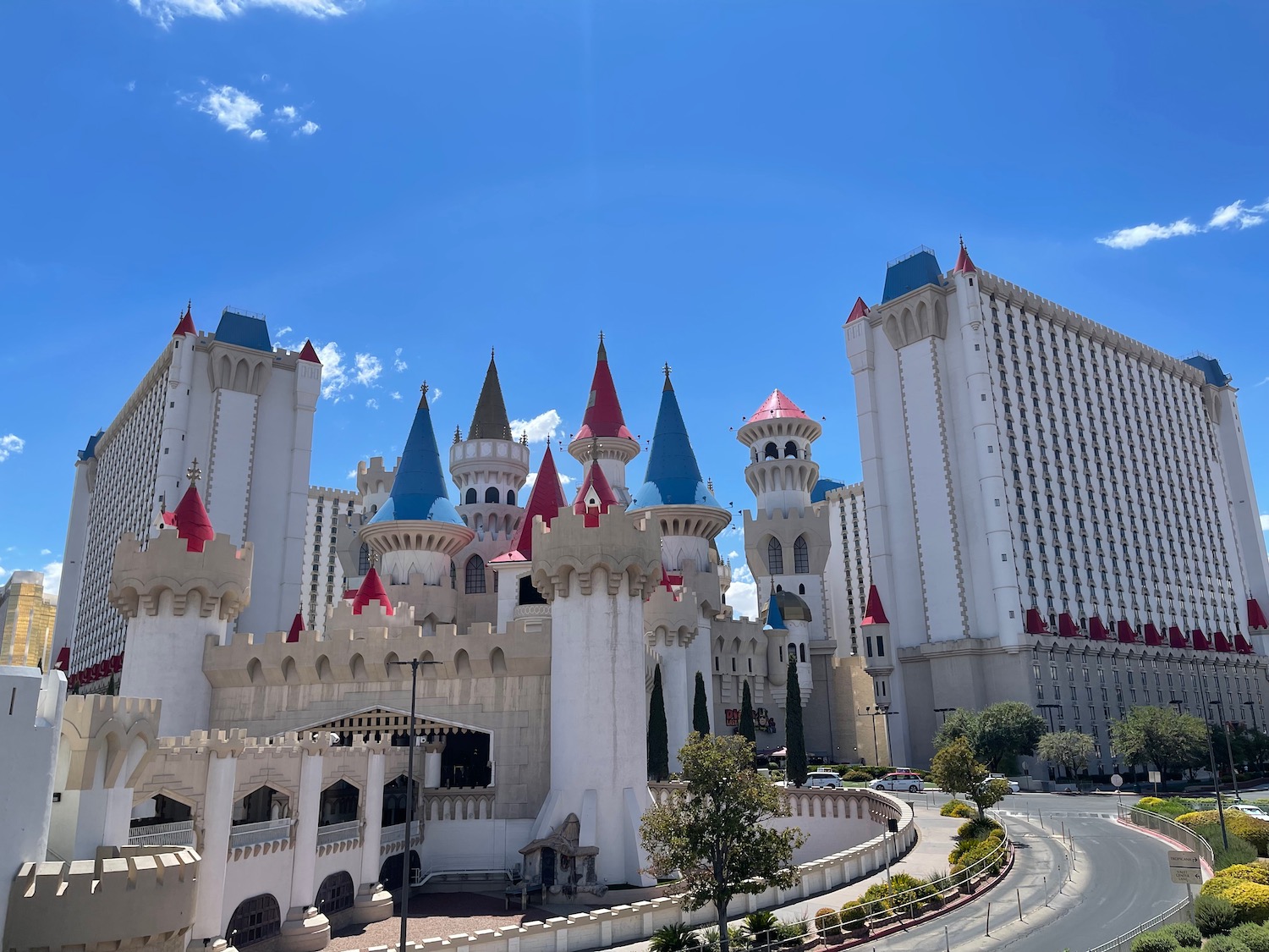 a large white castle with red and blue towers with Excalibur Hotel and Casino in the background
