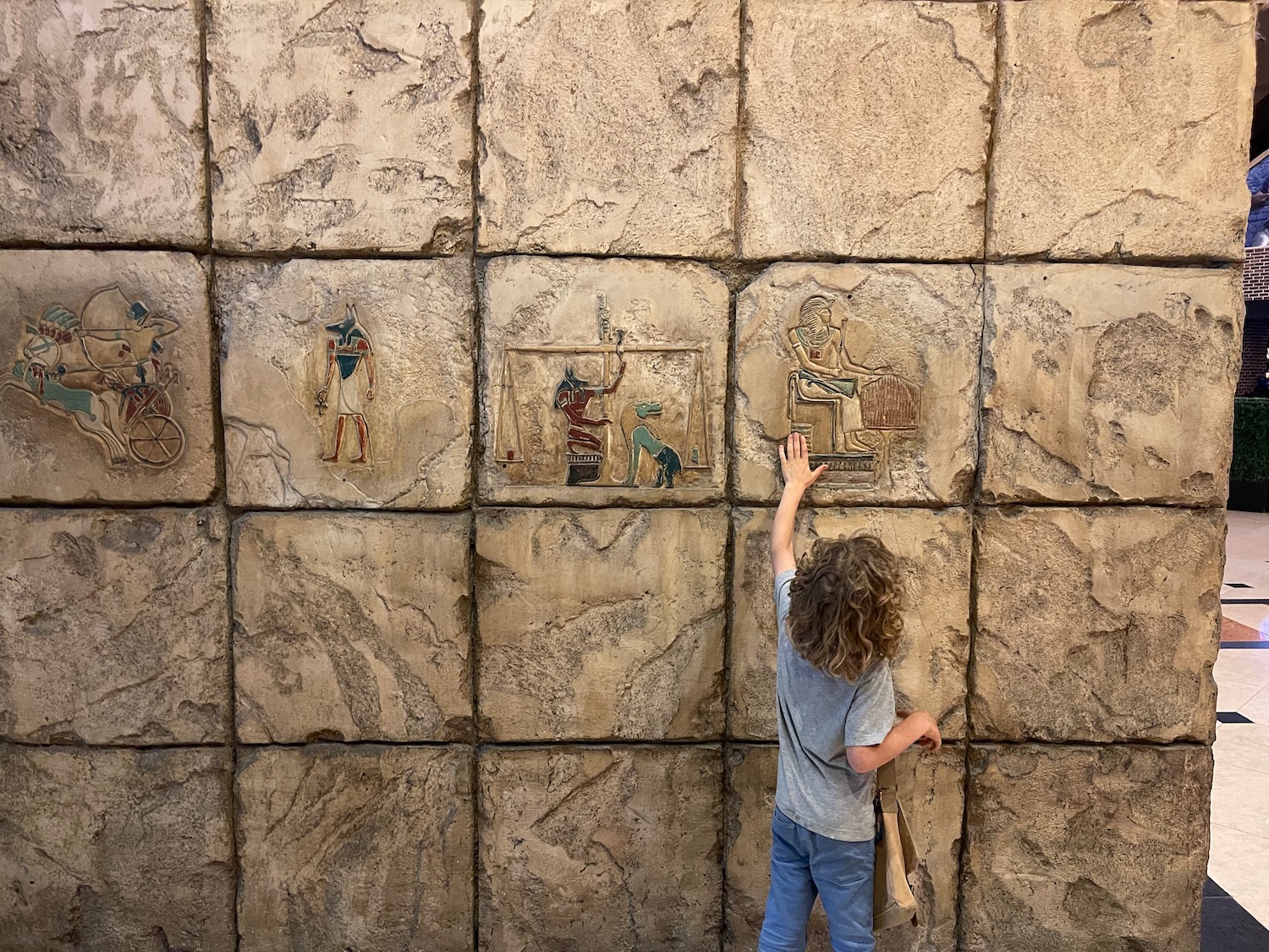 a child touching a wall with egyptian drawings