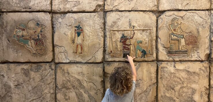 a child touching a wall with ancient egyptian art