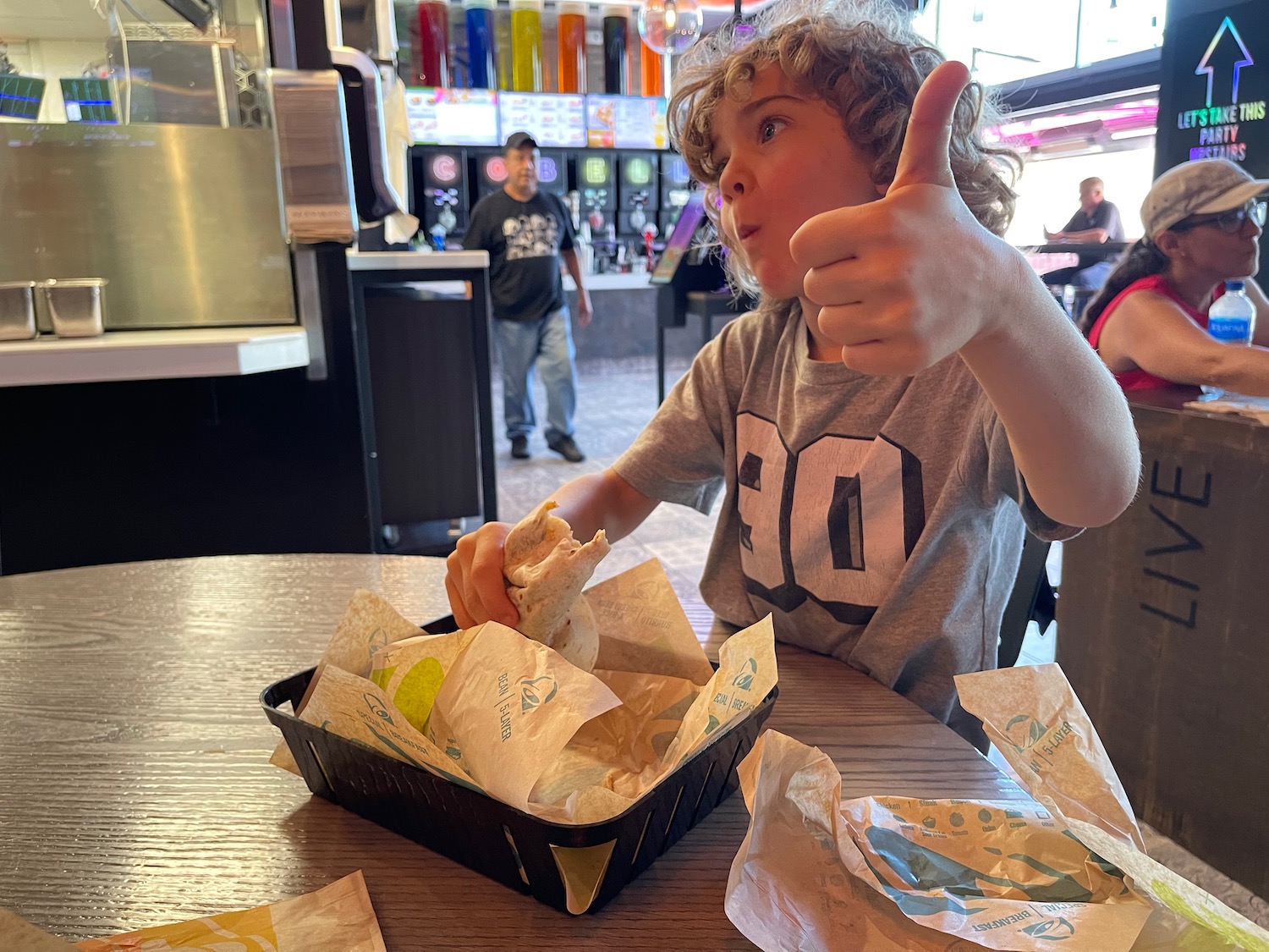 a boy holding up a thumbs up while eating tacos