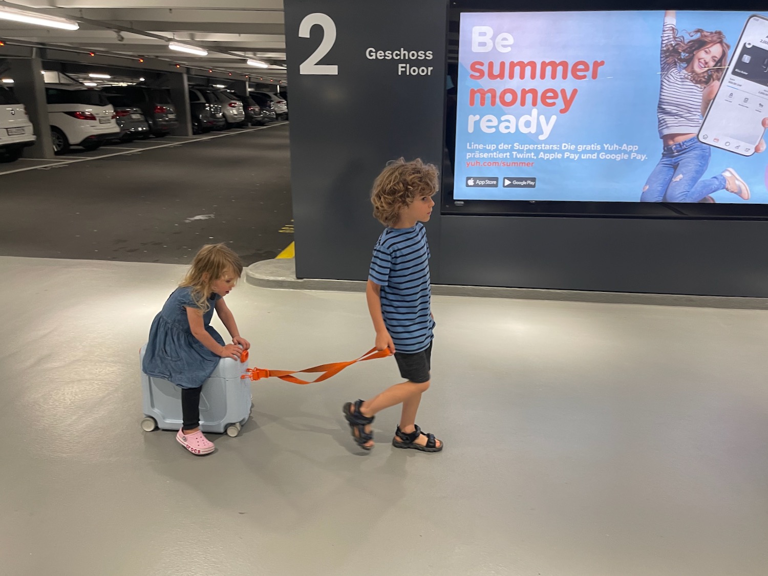 a boy and girl pulling luggage in a parking lot