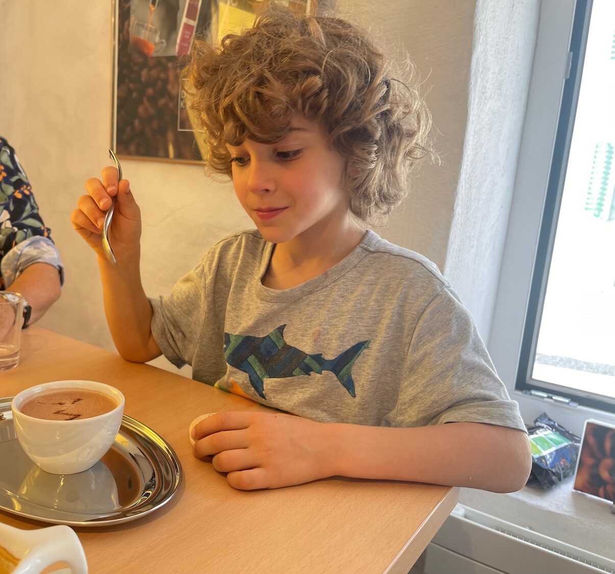 a boy sitting at a table with a cup of coffee and a spoon