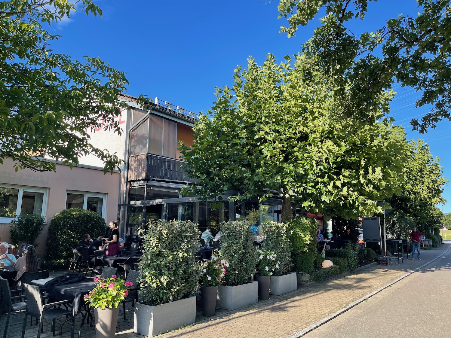 a sidewalk with a sidewalk and trees and people sitting at tables