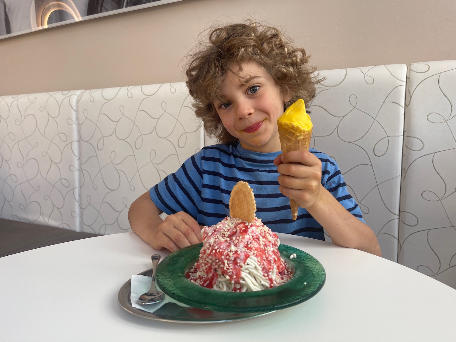 a boy sitting at a table with a plate of food and ice cream