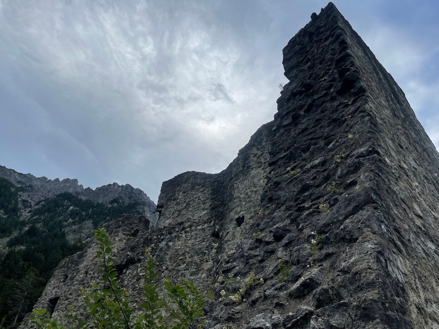 a rocky cliff with trees and clouds in the sky