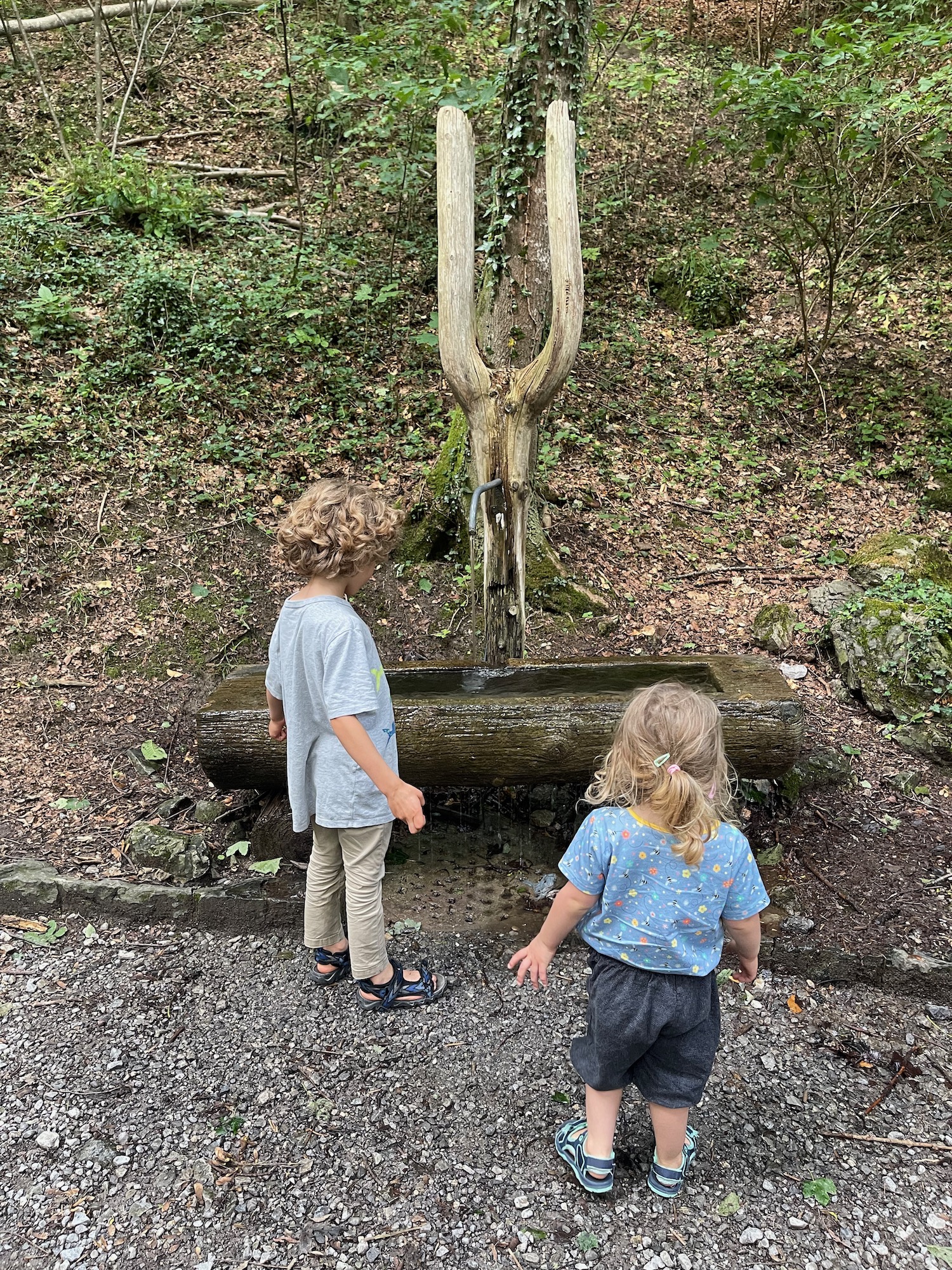 two children standing next to a water fountain