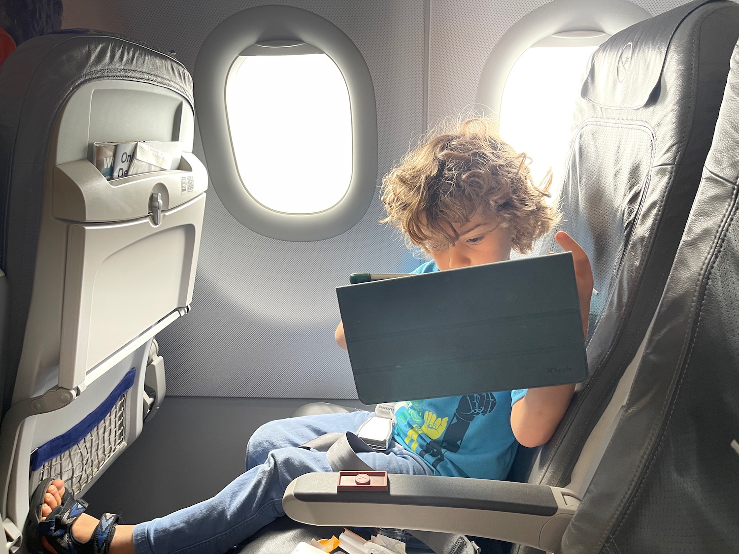 a child sitting in an airplane with a tablet