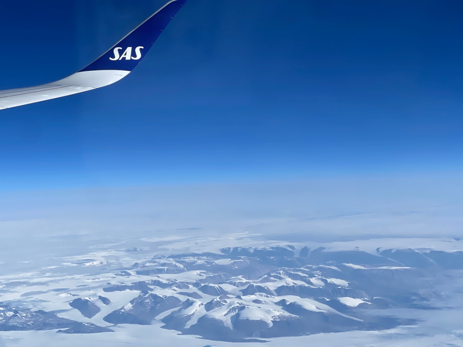 a plane wing with snow covered mountains in the background