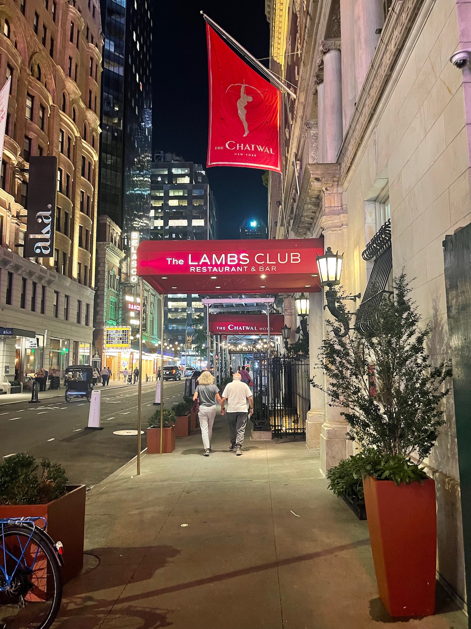 a couple of people walking down a sidewalk with a sign above them